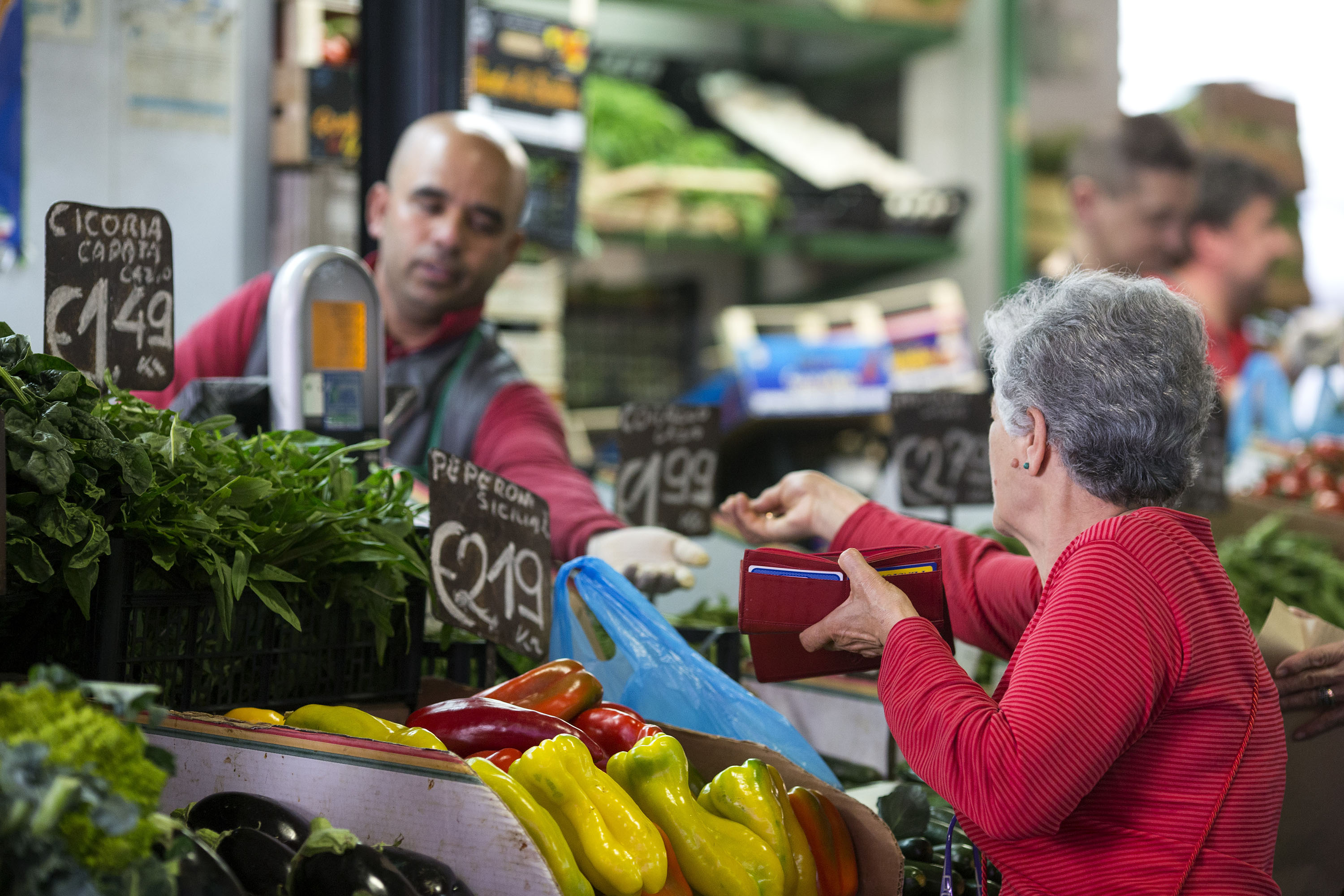 A customer buying fresh vegetables at a vegetable stall in a city market, Italy