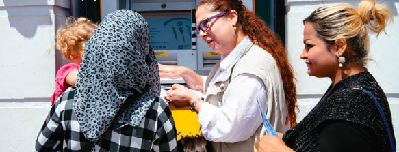 Following the issue of a cash distribution debit card, a Mercy Corps team member helps Walaa, 23, and her three children withdraw cash from an ATM.