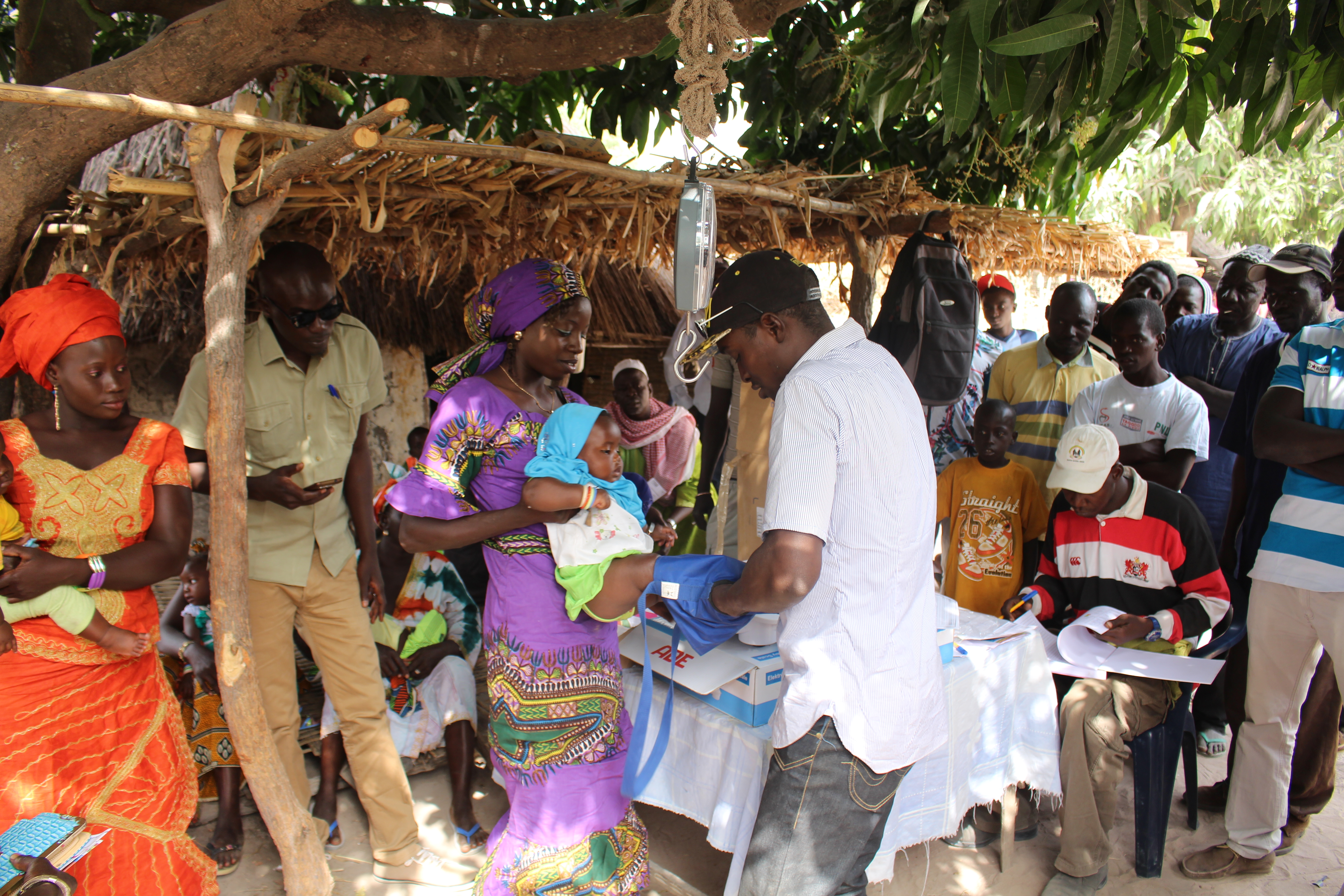Image shows a woman holding her baby whilst it is being prepped to be weighed at weighing station.