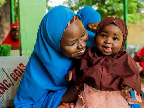 A woman in a blue hijab cradling a baby in her arms.