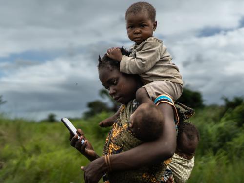 Woman carrying child on her back while on her phone
