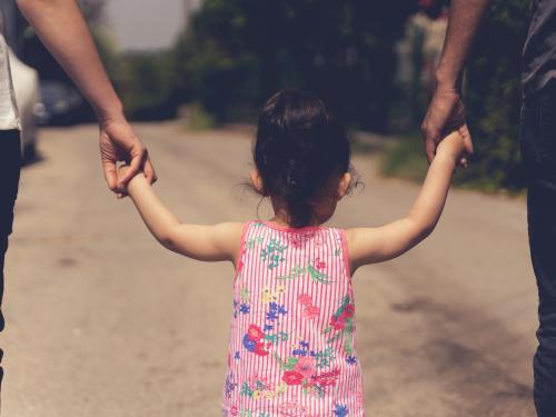 girl walking holding hands with adults on either side