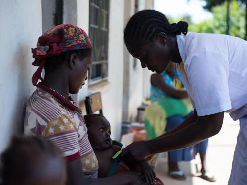 A mother holding her infant who is being checked by a medical professional