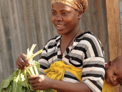 Woman carrying child on her back and holding vegetables in her hands