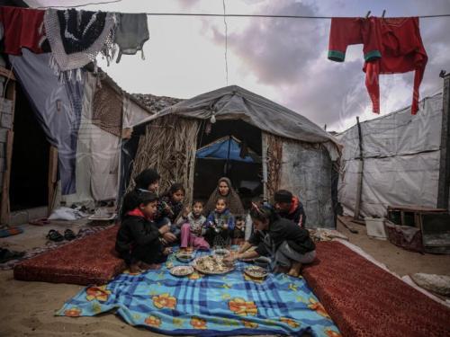 A family sitting eating outside of a tent in a refugee camp