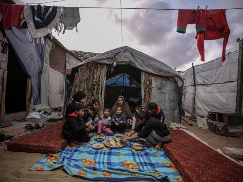 A family sitting eating outside of a tent in a refugee camp