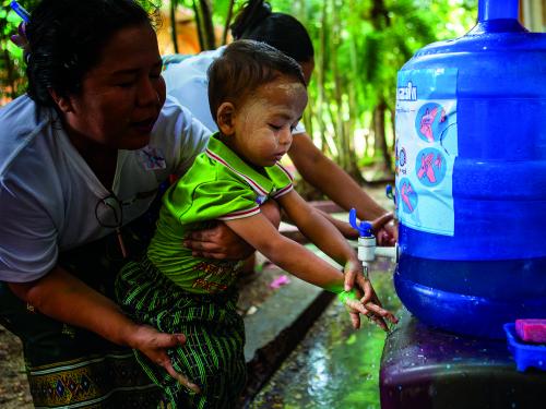 A little girl washes her hands under a tap