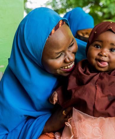 A woman in a blue hijab is holding a baby.