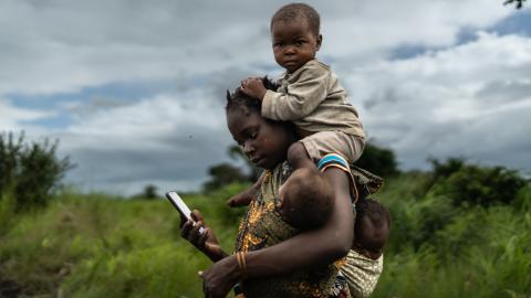 Woman carrying child on her back while on her phone