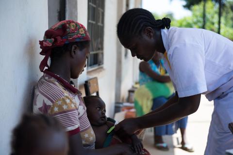 A mother holding her infant who is being checked by a medical professional