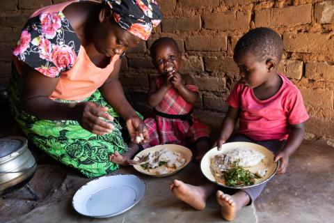 Mother and children are eating together sat on the floor