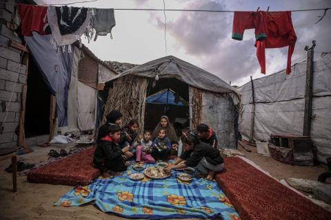 A family sitting eating outside of a tent in a refugee camp