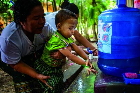 A little girl washes her hands under a tap